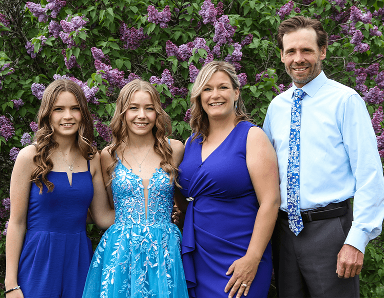 46 Lawn owners with their two teen daughters standing in front of lilac tree.